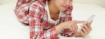 ベッドの上でスマホを操作する女性