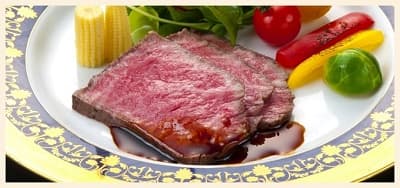 野菜と一緒にお皿に盛りつけられたソースのかかったローストビーフの切り身